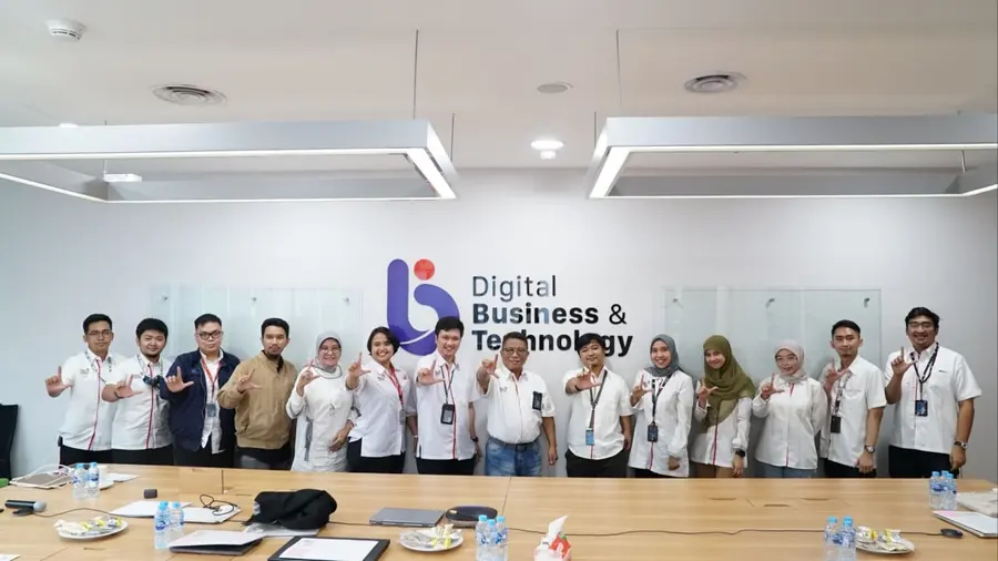 The Digital Business & Technology team lined up in a meeting room, each making the same hand sign