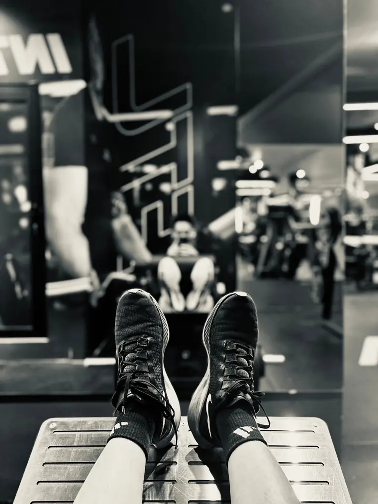 Black and white photo of sneakers resting on a leg press machine in a gym