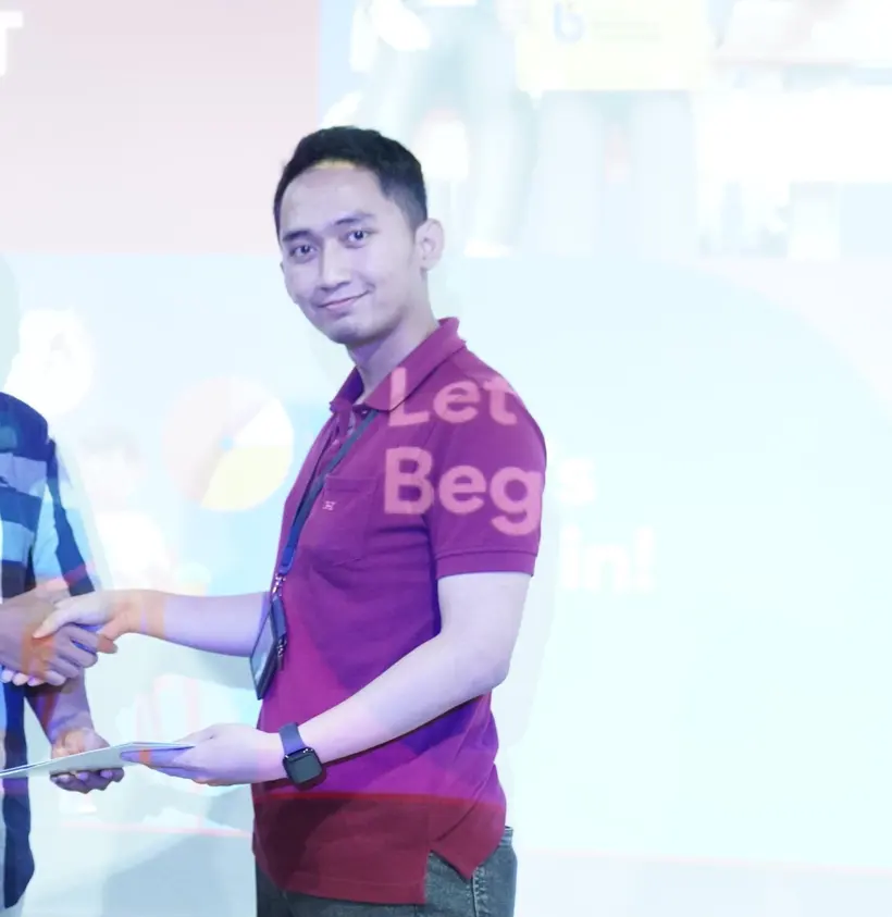 Adryan in a maroon polo shaking hands while receiving an envelope on stage