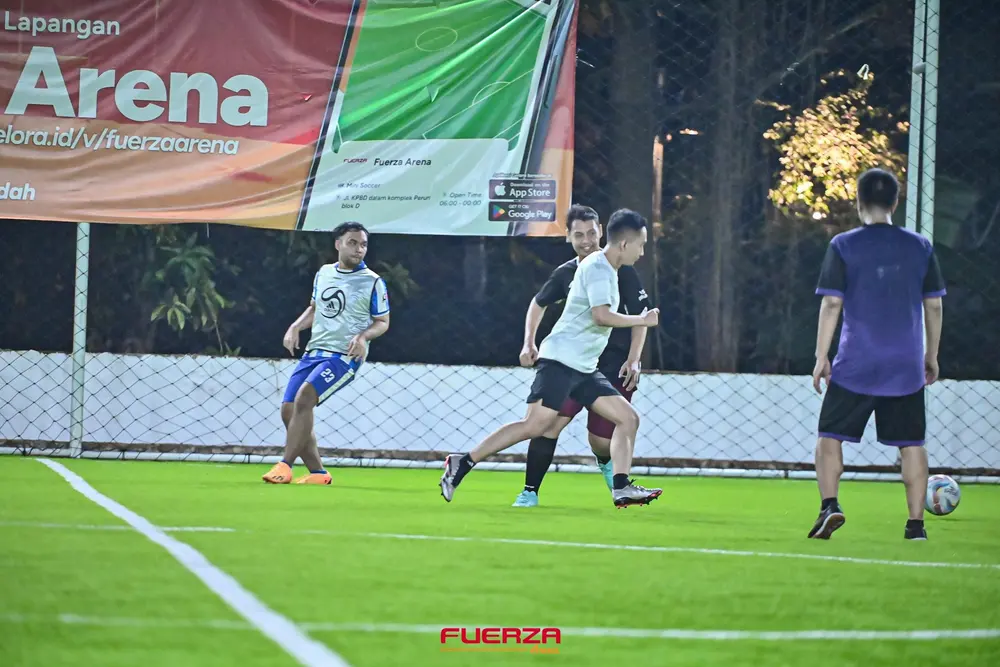 Four players moving across a mini soccer pitch at night