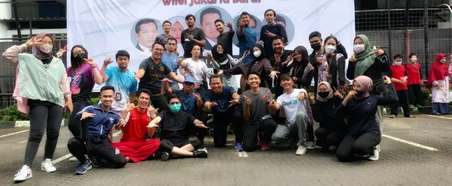 A large group of colleagues posing outdoors in front of a banner at Witel Jakarta Barat