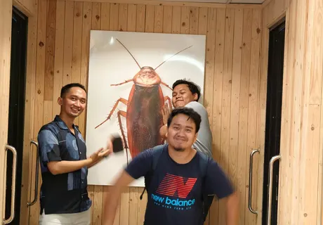 Alvin and two friends joking around in front of a cockroach poster